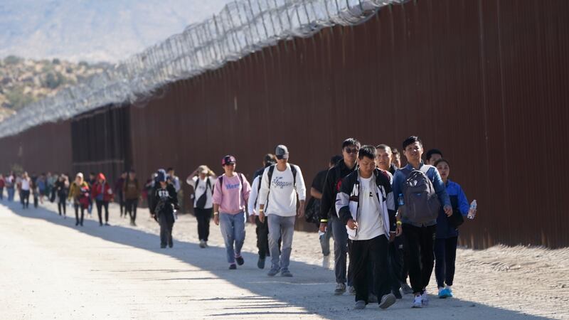 ARCHIVO - Un grupo de personas, incluidos muchos de China, camina junto al muro tras cruzar la...