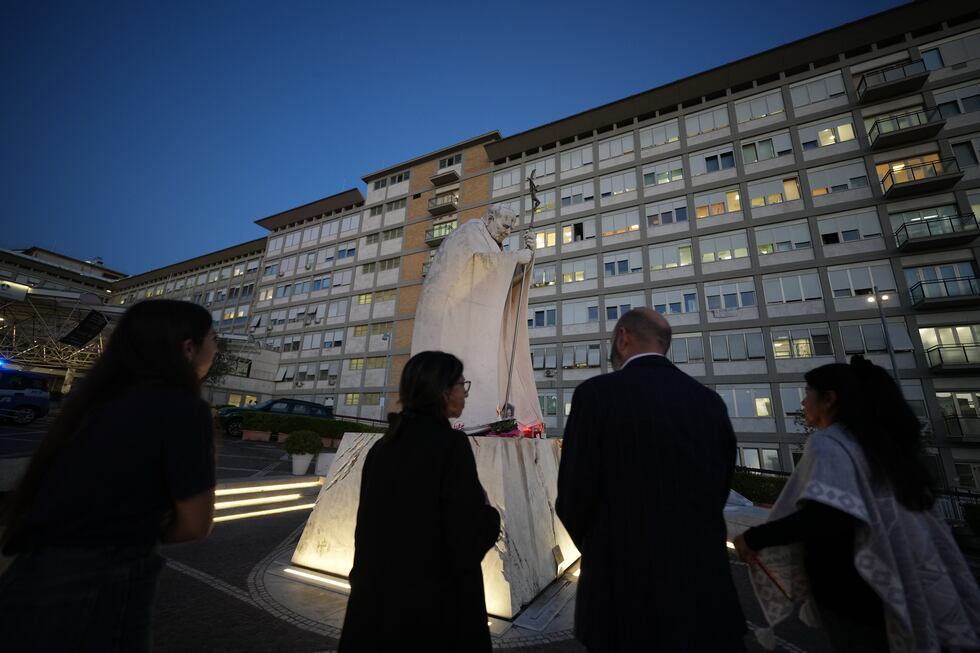 Varias personas se reúnen para rezar por el papa León XIV junto a una estatua del San Juan...